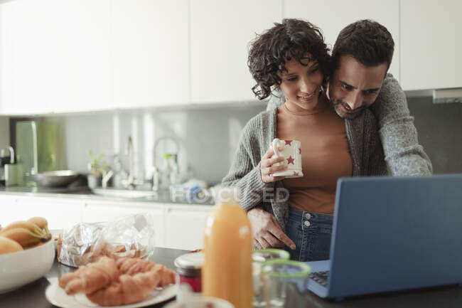 Casal afetuoso trabalhando no laptop na cozinha da manhã — Fotografia de Stock