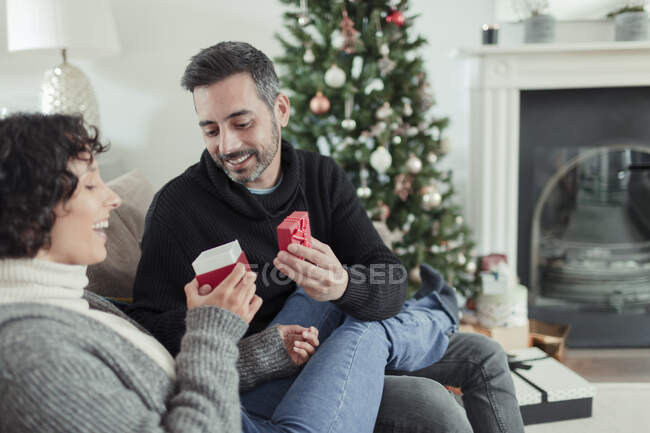 Feliz pareja abriendo regalo de Navidad en el sofá de la sala - foto de stock