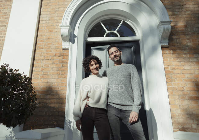 Portrait happy couple standing at front door on sunny house stoop — Stock Photo