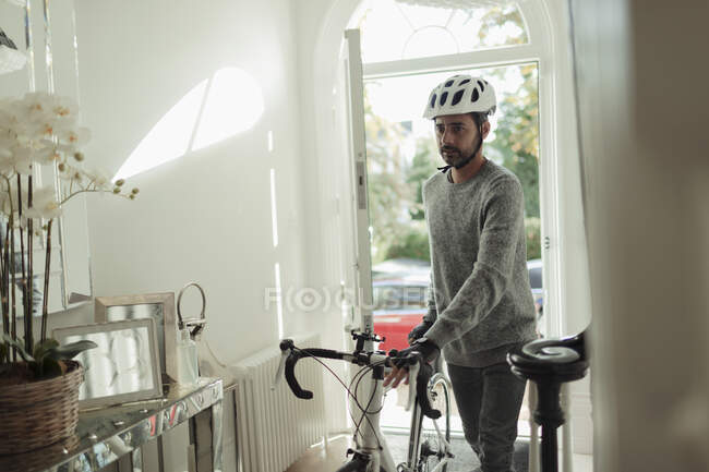 Человек у входной двери с велосипедом и велосипедным шлемом — стоковое фото