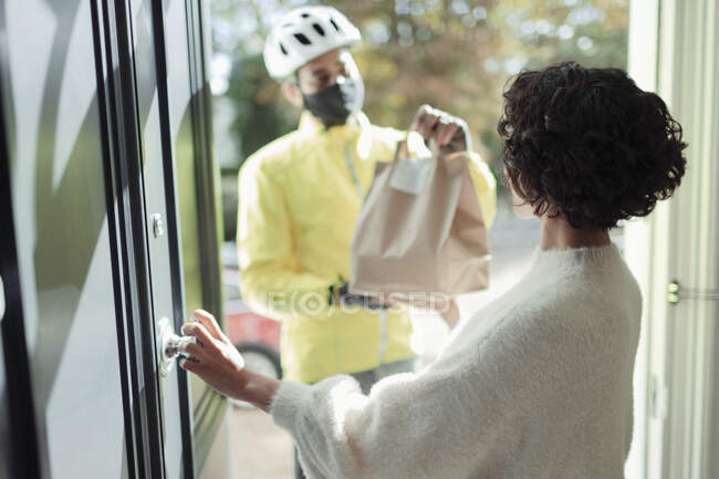 Donna che riceve la consegna di cibo da uomo in maschera davanti alla porta — Foto stock