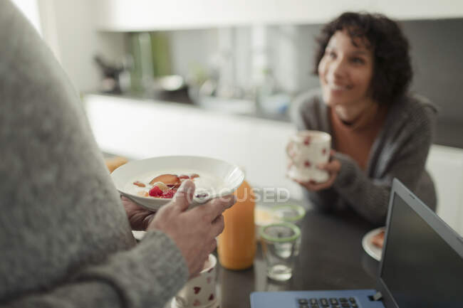 Couple eating breakfast and talking in morning kitchen with laptop — Stock Photo