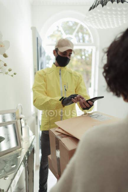 Woman receiving home delivery from man in mask with smart phone — Stock Photo