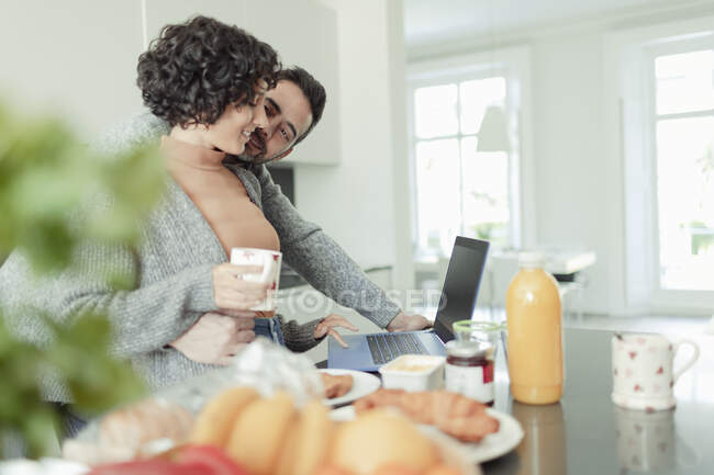 Casal afetuoso trabalhando no laptop na cozinha da manhã — Fotografia de Stock
