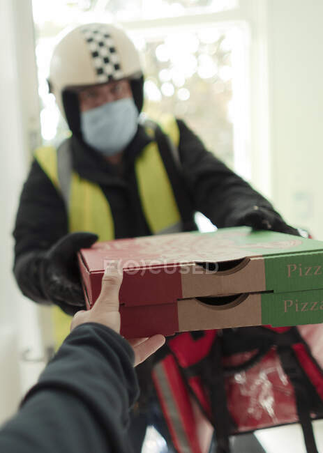 Чоловік у масці та шоломі доставляє піцу — стокове фото