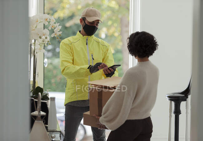 Woman receiving package from delivery man in face mask at front door — Stock Photo