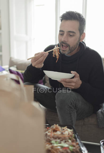 Hombre comiendo fideos para llevar con palillos - foto de stock