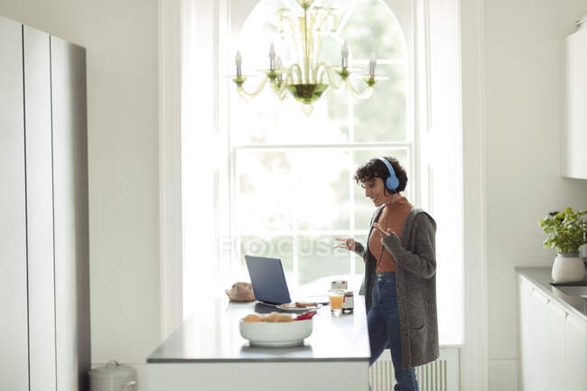 Mulher com fones de ouvido videoconferência no laptop na cozinha — Fotografia de Stock