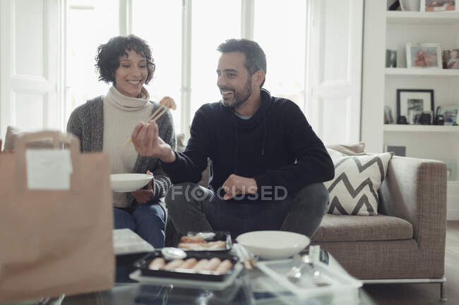 Joyeux couple mangeant de la nourriture à emporter avec des baguettes dans le salon — Photo de stock