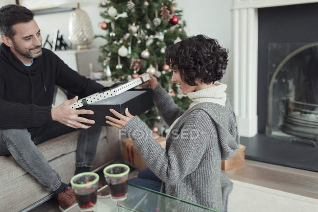 Esposa abriendo regalo de Navidad de marido en sala de estar - foto de stock