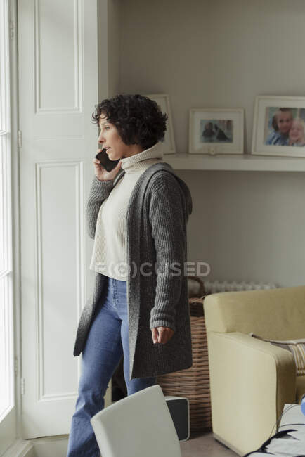 Frau telefoniert am Wohnzimmerfenster mit Smartphone — Stockfoto
