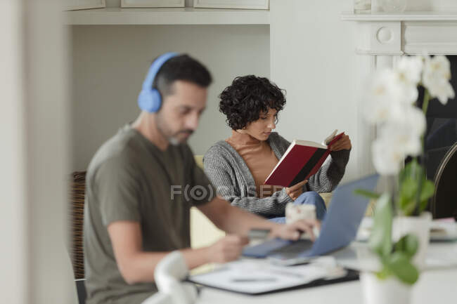 Pareja leyendo y trabajando desde casa en el portátil - foto de stock