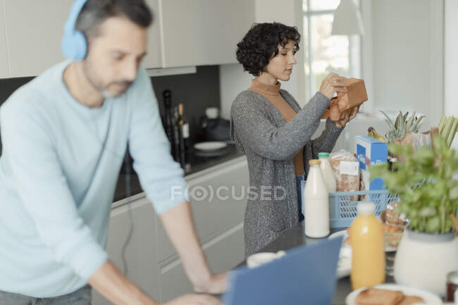 Пара работает из дома и разгружает продукты на кухне — стоковое фото