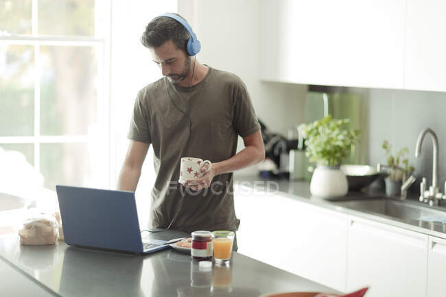 Чоловік з навушниками, що працюють з дому на ноутбуці на кухні — стокове фото