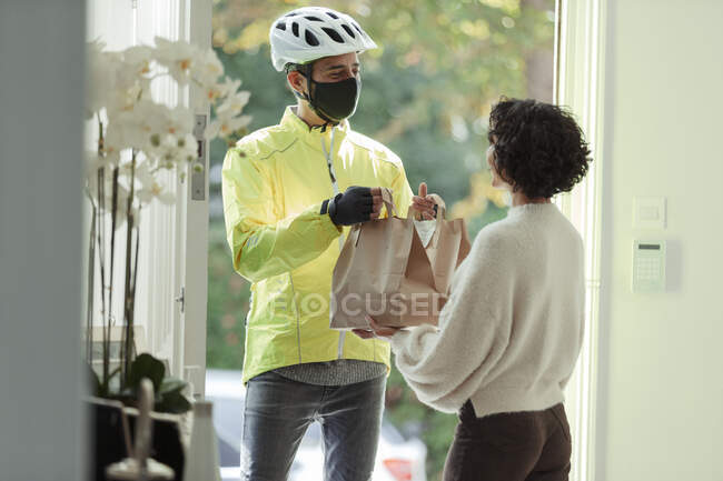 Mulher recebendo entrega de alimentos de homem em máscara facial e capacete — Fotografia de Stock