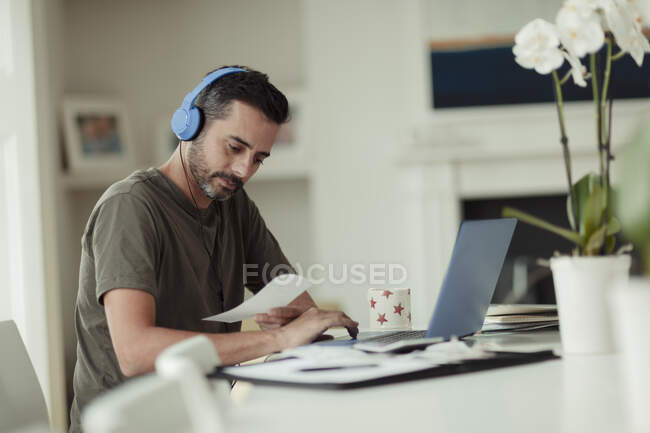 Hombre con auriculares y recibos pagando facturas en el portátil - foto de stock