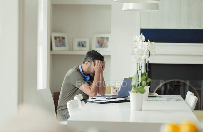 Homme fatigué avec la tête dans les mains travaillant de la maison à l'ordinateur portable — Photo de stock