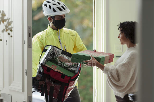 Женщина получает доставку пиццы от курьера в маске на входной двери — стоковое фото