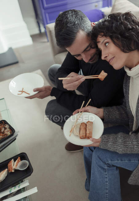 Verspielter Ehemann füttert Ehefrau mit Essstäbchen mit Eierrolle — Stockfoto