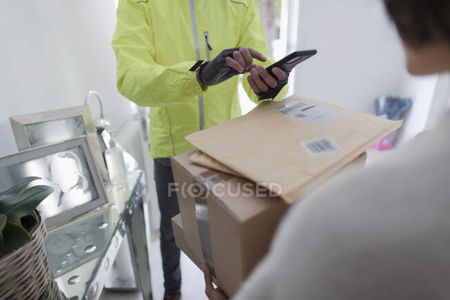 Mulher recebendo pacotes de homem de entrega com telefone inteligente — Fotografia de Stock