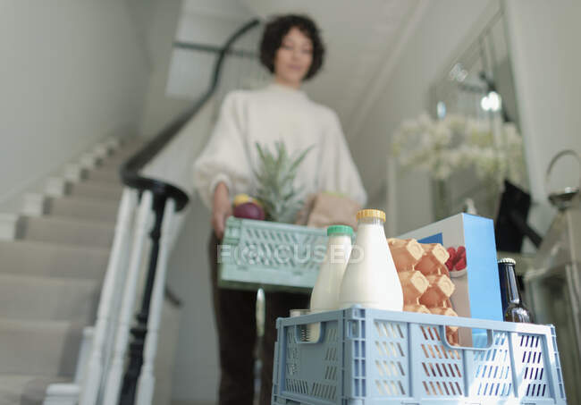 Woman receiving grocery delivery crates in foyer — Stock Photo