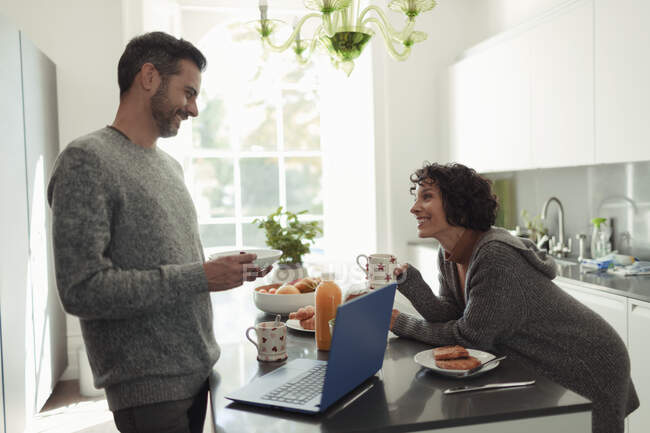 Couple heureux appréciant le petit déjeuner et travaillant à l'ordinateur portable dans la cuisine — Photo de stock