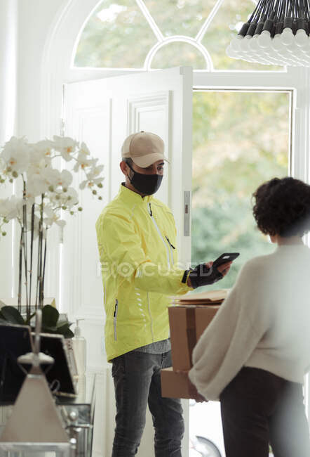 Courier in face mask delivery packages to woman at home — Stock Photo