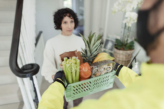 Woman receiving grocery delivery from courier in face mask — Stock Photo