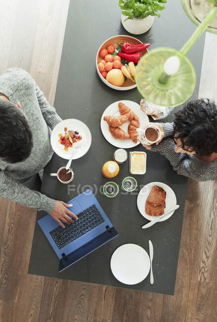Couple enjoying breakfast and working at laptop in morning kitchen — Stock Photo