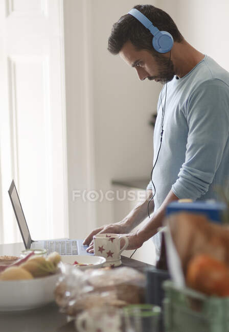 Man with headphones working from home at laptop in morning kitchen — Stock Photo