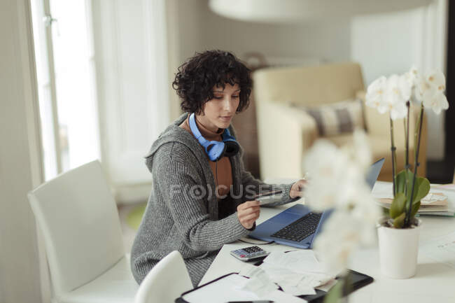 Woman with credit card paying bills at laptop at dining table — Stock Photo