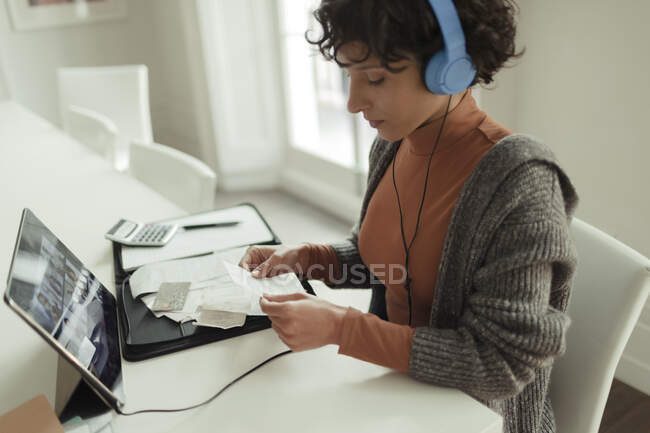 Mulher com fones de ouvido e recibos pagando contas em tablet digital — Fotografia de Stock