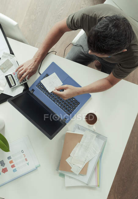 Hombre con recibos y calculadora pagando facturas en el portátil - foto de stock