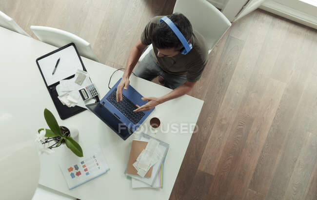 Homem com fones de ouvido trabalhando em casa no laptop na mesa de jantar — Fotografia de Stock
