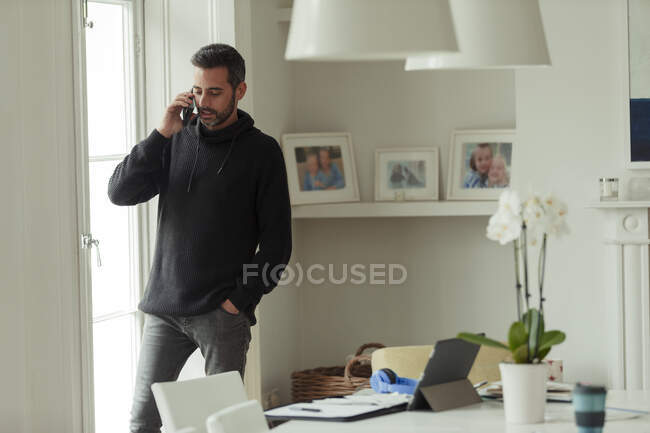 Человек, работающий из дома, разговаривает по смартфону у окна — стоковое фото