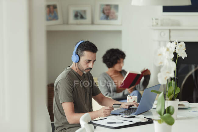 Man with headphones and credit card paying bills at laptop — Stock Photo