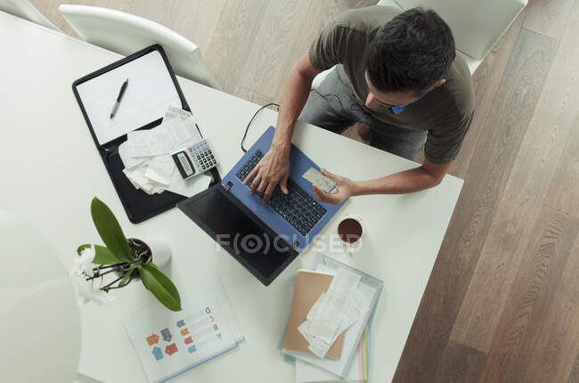 Чоловік з кредитною карткою платить рахунки за ноутбук на обідньому столі — стокове фото
