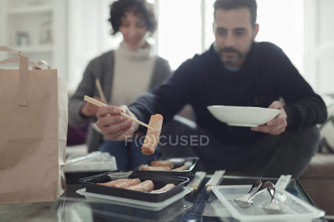 Couple enjoying egg roll takeout food with chopsticks in living room — Stock Photo