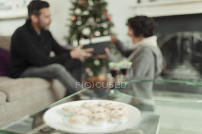 Frau öffnet Weihnachtsgeschenk ihres Mannes hinter Tablett mit Hackfleischkuchen — Stockfoto
