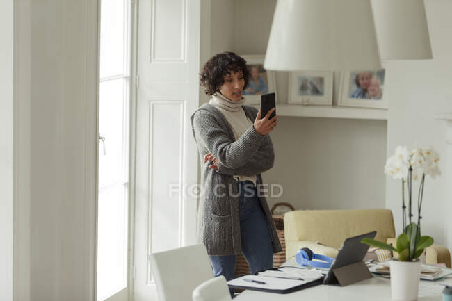 Mulher com telefone inteligente trabalhando em casa na janela — Fotografia de Stock