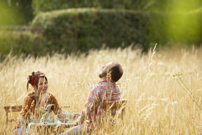 Happy couple laughing at table in field of sunny tall grass — Stock Photo