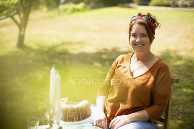 Retrato mujer feliz disfrutando de la torta en la mesa en el soleado jardín de verano - foto de stock