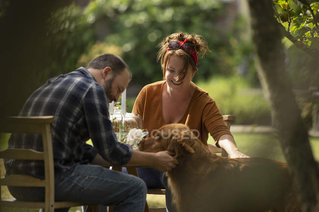 Pareja feliz con Golden Retriever perro en la mesa del jardín - foto de stock