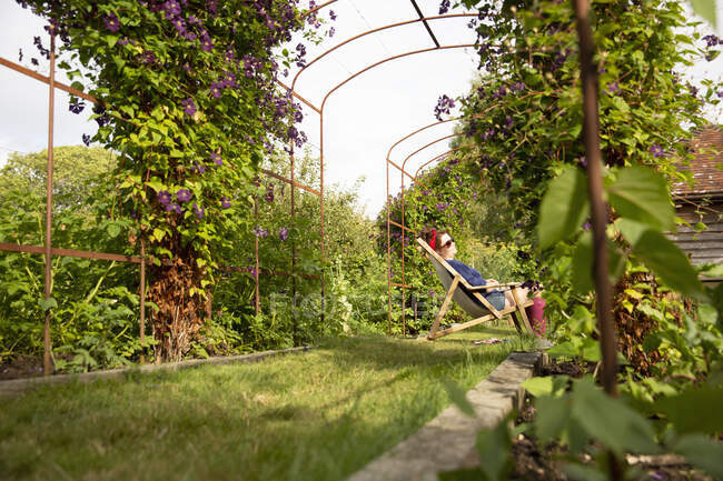 Serena mulher relaxante na cadeira de gramado no jardim de verão ensolarado — Fotografia de Stock