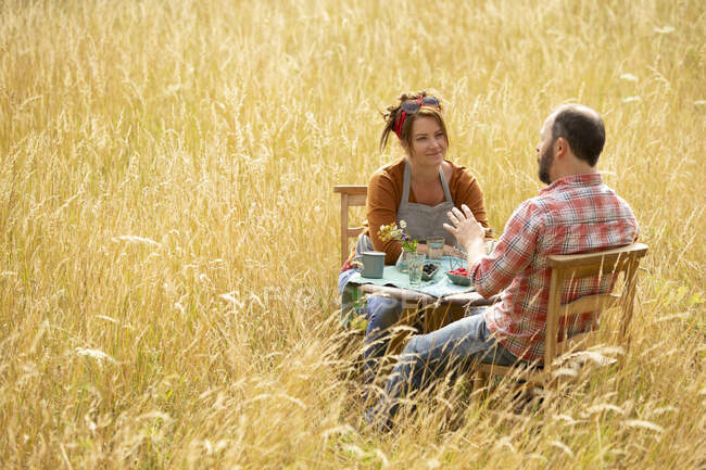 Couple talking and eating berries at table in sunny tall grass — Stock Photo