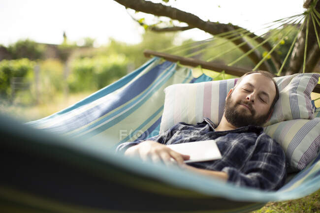 Serene man with digital tablet sleeping in backyard summer hammock — Stock Photo