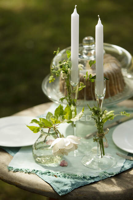Candlesticks and rose on garden table with cake — Stock Photo