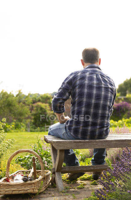 Uomo in pausa dal giardinaggio in panchina nel soleggiato giardino estivo — Foto stock