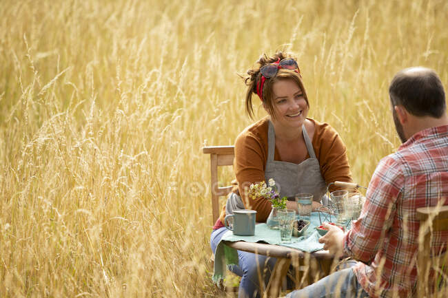 Счастливая пара разговаривает за столом в солнечной летней высокой траве — стоковое фото