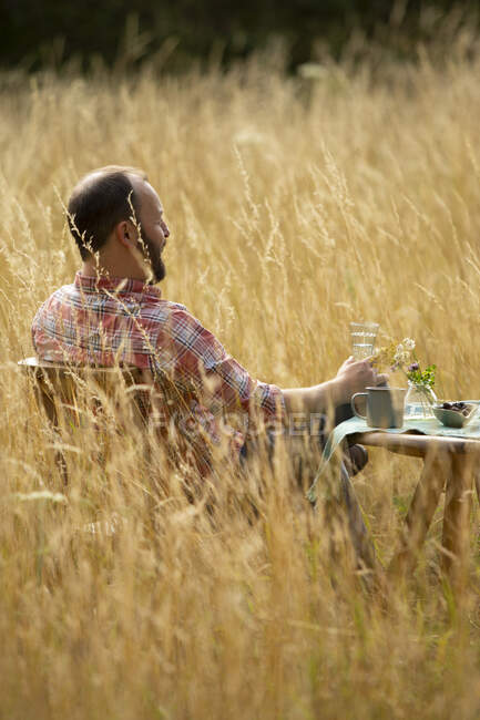 Человек расслабляется за столом в солнечной летней высокой траве — стоковое фото